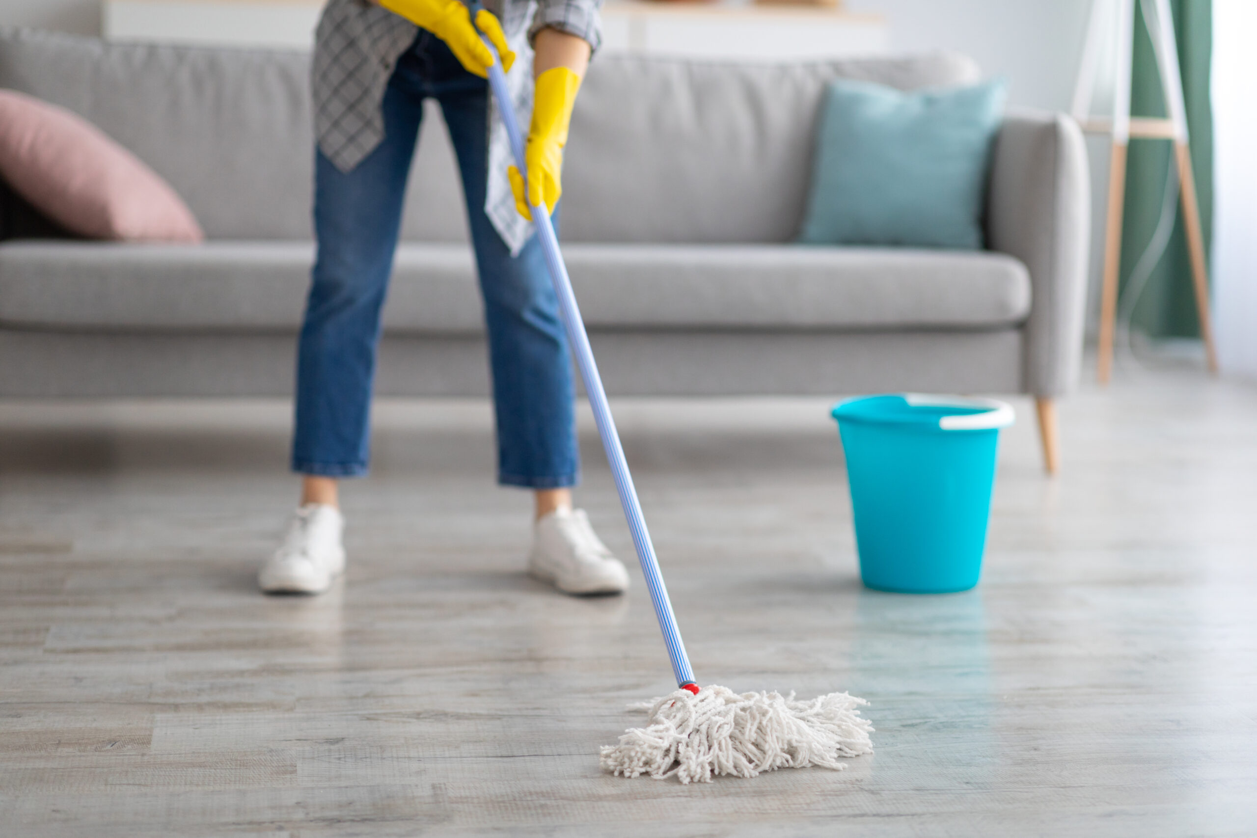 Person mopping a clean hardwood floor in a modern living room with a bucket nearby.